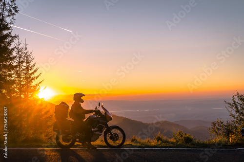 Silhouette of man biker and adventure motorcycle on the road with sunset light background. Top of mountains, tourism motorbike, vacation active lifestyle. Transfagarasan, Romania.