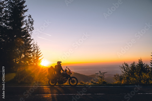Silhouette of man biker and adventure motorcycle on the road with sunset light background. Top of mountains, tourism motorbike, vacation active lifestyle. Transfagarasan, Romania.