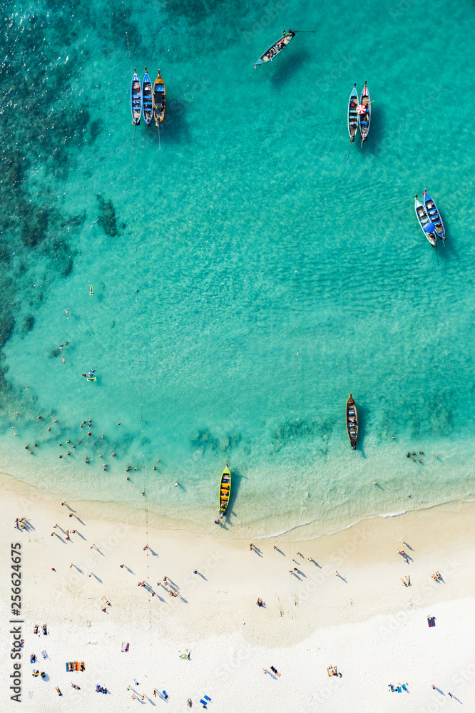 View from above, aerial view of a beautiful tropical beach with white sand and turquoise clear water, long tail boats and people sunbathing, Freedom beach, Phuket, Thailand.