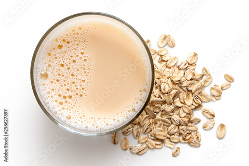 Glass of oat drink  next to a pile of dry oats isolated on white from above.