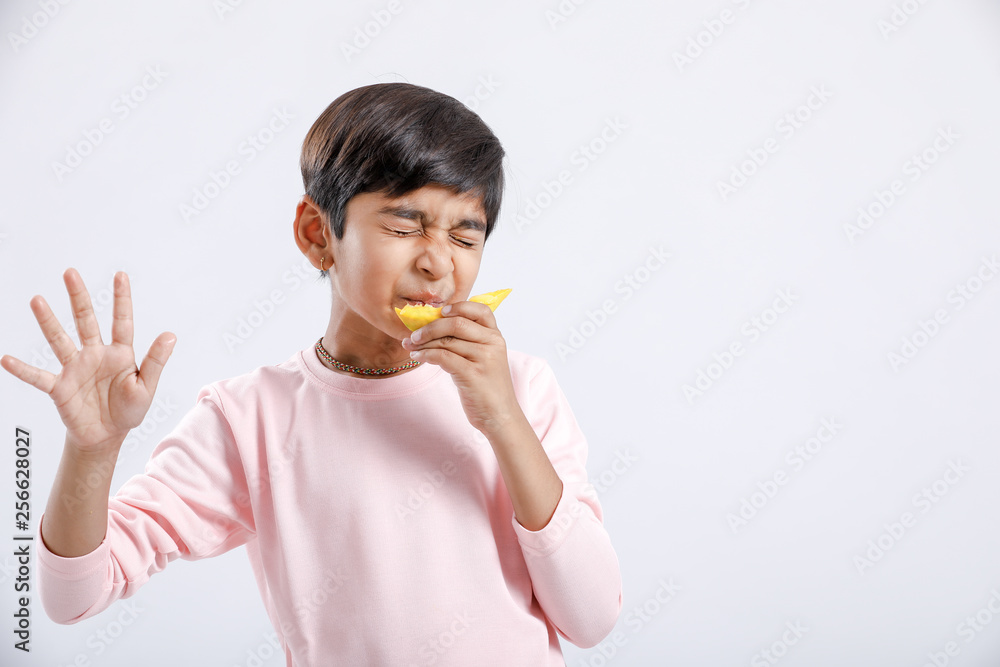 Cute indian/Asian little boy eating Mango with multiple expressions. isolated over white background Cute indian/Asian little boy eating Mango with multiple expressions. isolated over white background