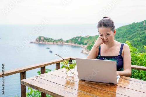 Asian young lady stressfully working online with background of sea view from balcony above sea level height