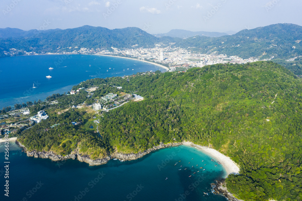 Fototapeta premium View from above, stunning aerial view of Patong city skyline in the distance and the beautiful Freedom Beach bathed by a turquoise and clear sea in the foreground, Phuket, Thailand.