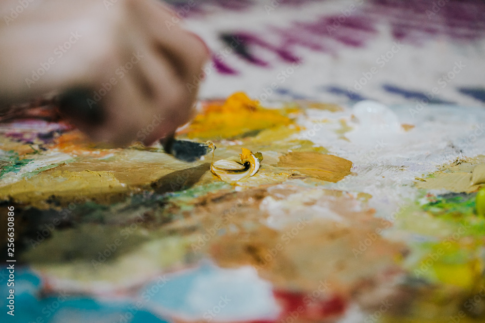 .Young and pretty artist creating new paintings in her bright and colored studio. Relaxed, inspired and creative. Detail photo of the spatula in the color palette. Lifestyle .Young and pretty artist creating new paintings in her bright and colored studio. Relaxed, inspired and creative. Detail photo of the spatula in the color palette. Lifestyle