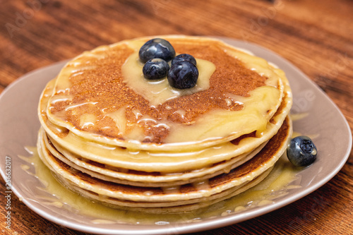 Pancakes with blueberries and honey on the dark brown wooden background