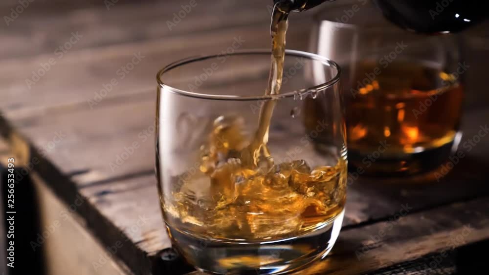 Golden whiskey pouring in the glass from the bottle. With ice cubes. Golden whiskey pouring in the glass from the bottle. With ice cubes.