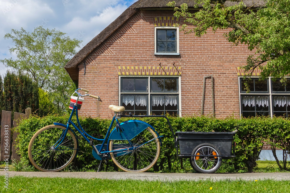Parking bike with trolley in front of the house with brick wall, classic living in Giethoorn Parking bike with trolley in front of the house with brick wall, classic living in Giethoorn