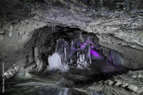 Underground glacier in Glaciers Cave in Apuseni mountains, Scarisoara, Romania. Ice and big icicles with colorful back light. Stalactites and stalagmites in dark cave