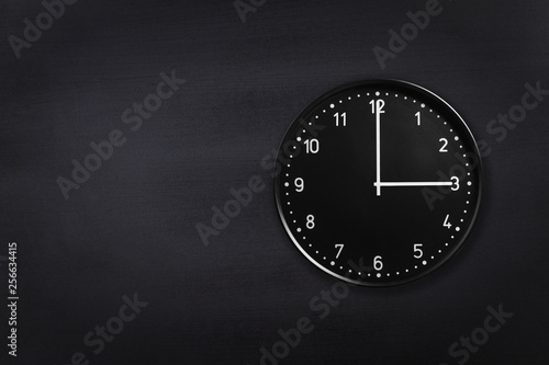 Black wall clock showing three o'clock on black chalkboard background. Office clock showing 3am or 3pm on black texture