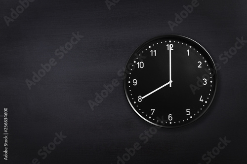 Black wall clock showing eight o'clock on black chalkboard background. Office clock showing 8am or 8pm on black texture