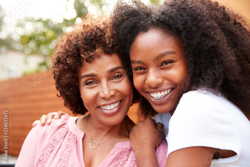 Middle aged black mum and teenage daughter embracing and smiling to camera