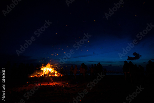 Large burning bonfire with soft glowing flame and sparkles flying all around. Romantic summer evening  people relaxing and enjoying calmness at the seaside during the Night of ancient lights.  