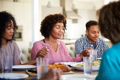 Woman sitting at the table holding hands with her young adult children saying grace before dinner