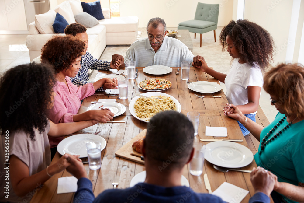 Three generation black family holding hands and saying grace at table before dinner,elevated view Three generation black family holding hands and saying grace at table before dinner,elevated view