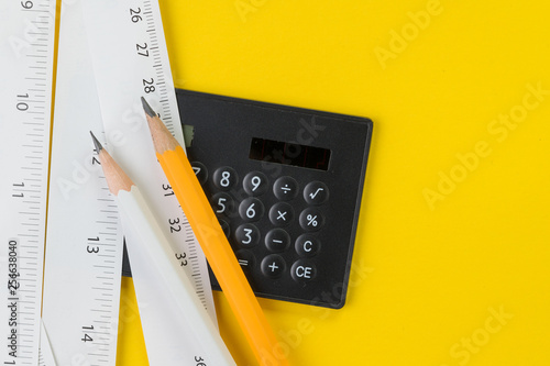 Calculator, pencils and white measuring tapes with centimetre and inches on vivid yellow background, length, long or maker instrument and enginerring tools concept photo