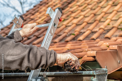 Foto Man on a ladder cleaning house gutters