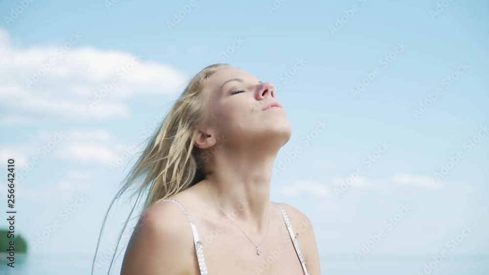 close pretty blond girl with long hair in swimsuit shakes head against boundless blue sky with white clouds slow motion close pretty blond girl with long hair in swimsuit shakes head against boundless blue sky with white clouds slow motion