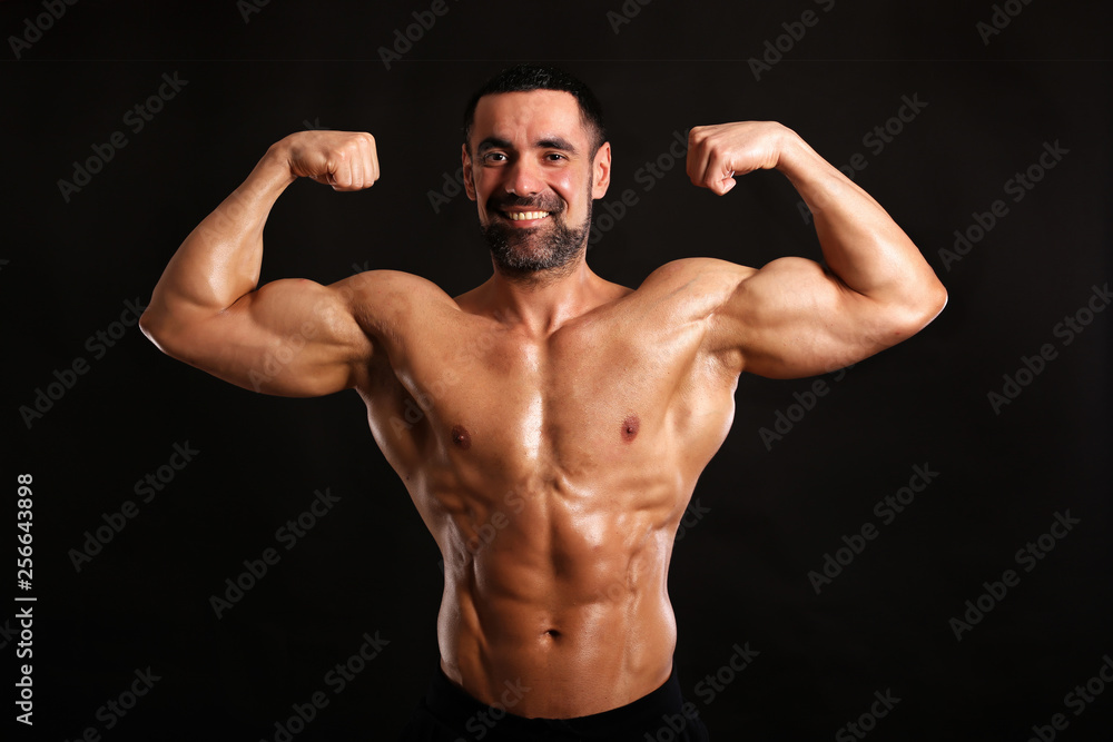 muscular man flexing his muscles on black background and smiling 