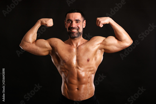 muscular man flexing his muscles on black background and smiling 