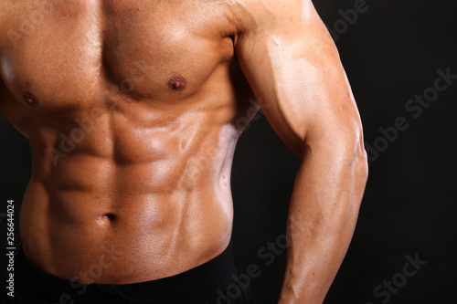 Portrait of young handsome muscular bodybuilder on black background torso close up view 