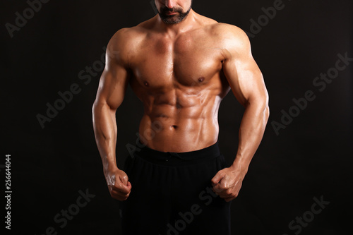 Portrait of young handsome muscular bodybuilder on black background torso close up view 