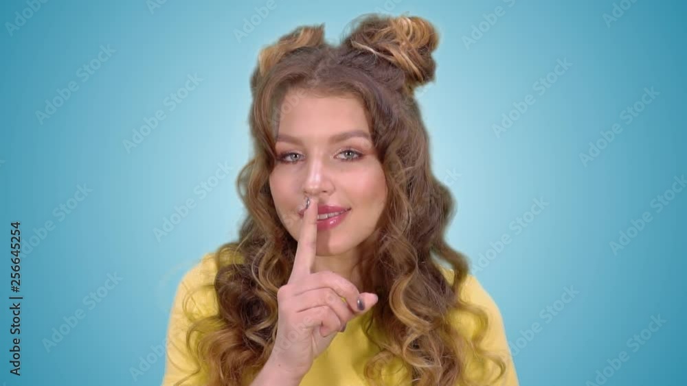 beautiful young girl in a yellow vest puts a finger to her lips and shows a gesture of silence and smiling while looking at the camera beautiful young girl in a yellow vest puts a finger to her lips and shows a gesture of silence and smiling while looking at the camera