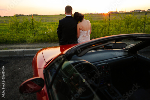 Beautiful wedding couple watching the sunset in a convertible car.