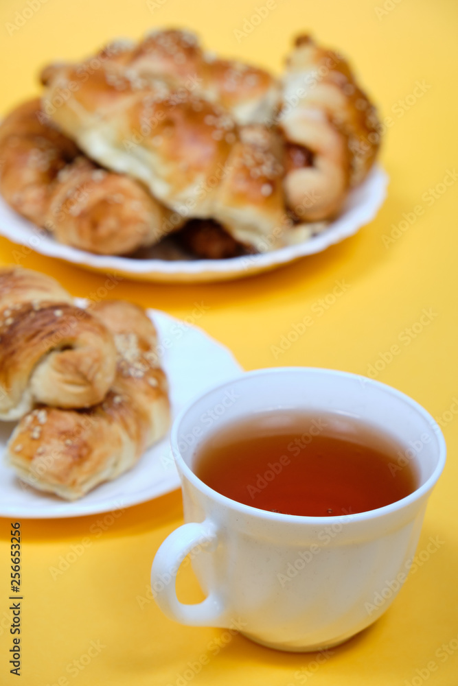 croissants on a white plate with a Cup of tea on a yellow background croissants on a white plate with a Cup of tea on a yellow background