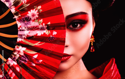 Wall Mural beautiful Japanese girl in kimono with a fan on a black background