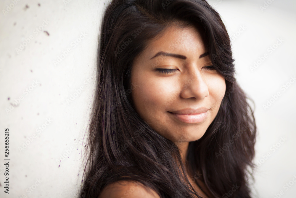 Young Spanish woman smiling at the camera. She is leaning against a wall eyes closed. Isolated on white. Young Spanish woman smiling at the camera. She is leaning against a wall eyes closed. Isolated on white.