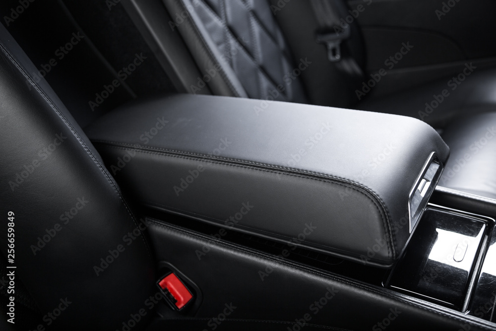 Close up of armrest between passenger seats of black leather car interior