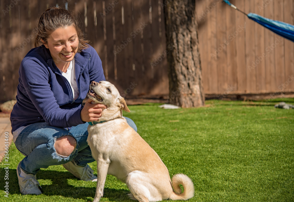 Pretty girl petting a happy white dog with a curly tail in a backyard with a hammock in the background.