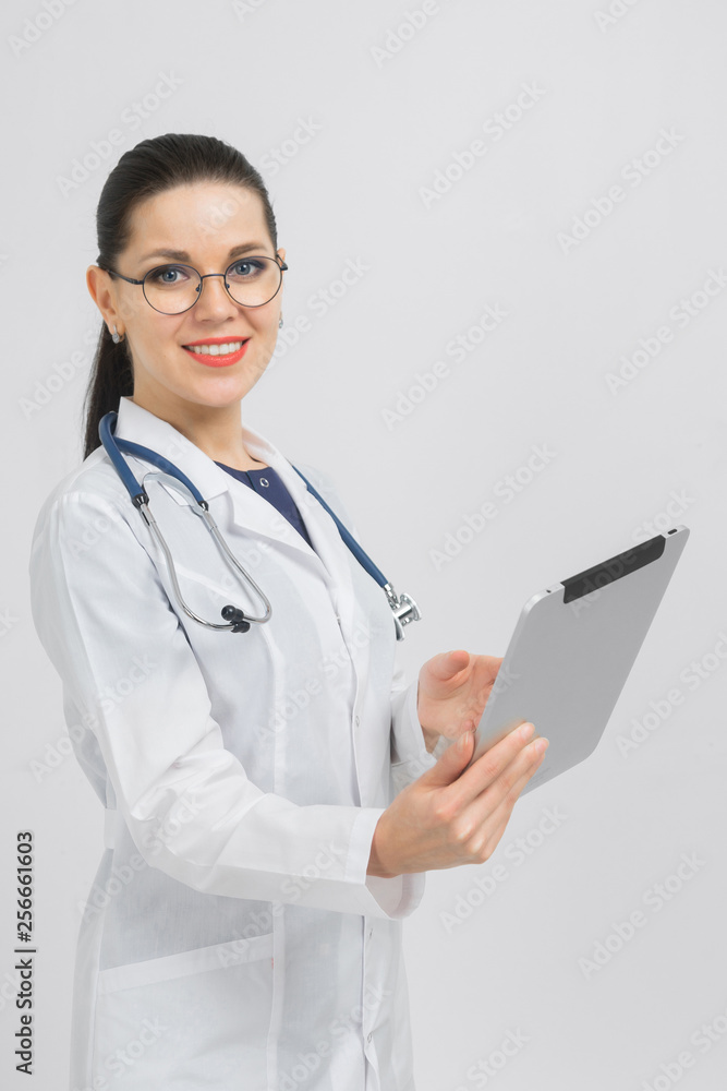 Portrait of brunet in doctors costume with a modern tablet in her hands isolated on background Portrait of brunet in doctors costume with a modern tablet in her hands isolated on background