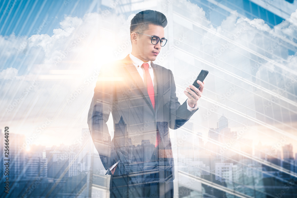 Fototapeta premium The double exposure image of the businessman using a smartphone during sunrise overlay with cityscape image. The concept of modern life, business, city life and internet of things.