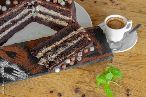 A chocolate cake with nuts wrapped in white and black chocolate. and a cup of coffee on a wooden background. With a sprig of mint and coffee beans. © Petia