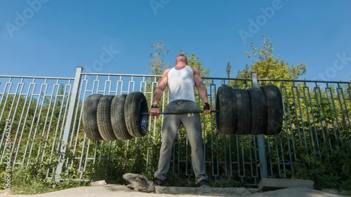 Strong man is deadlifting outdoor the DIY whells barbell. photo