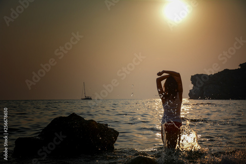 silhoueete of girl with waves crash on her figure in sunset light with ship on horizont photo