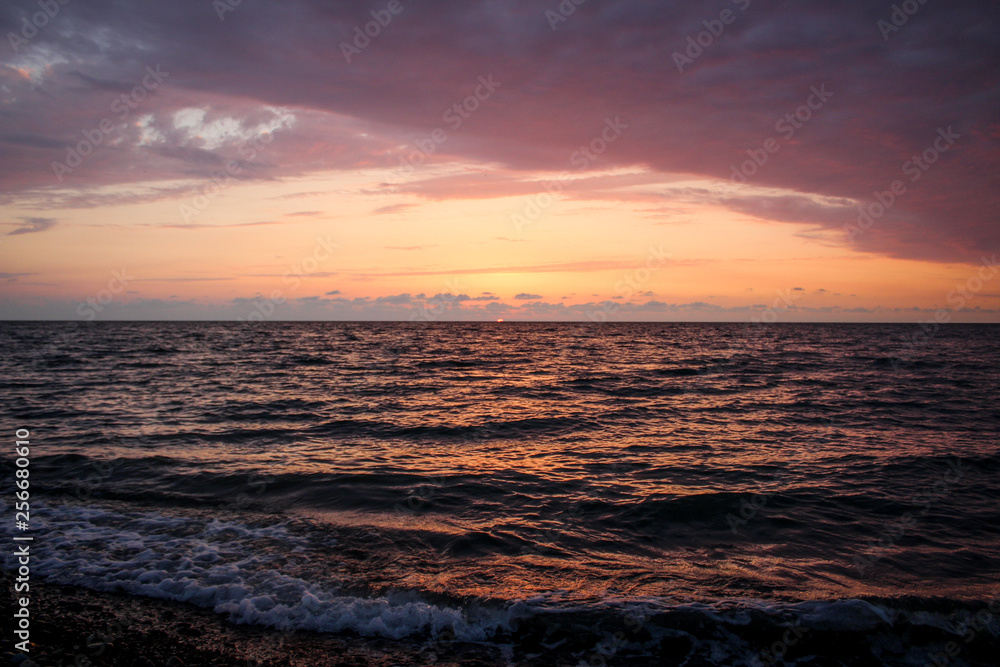 Golden, Fiery sunset on the Black Sea, on the beach. Coast, stones, waves, sun, beautiful sky, clouds. August, Batumi, Georgia. Water, lightness, play. Pink, lilac, crimson
