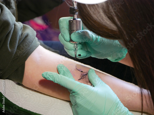 tattoo master makes a tattoo. close-up of hands and typewriter. green gloves