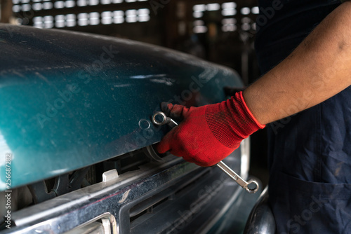 Arm of mechanic holding a spanner opening the bonnet of a car - Low point of view of a auto technician starting a repair on a vehicle