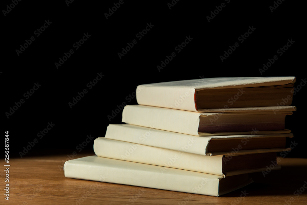 pile of books in white covers on wooden table isolated on black pile of books in white covers on wooden table isolated on black