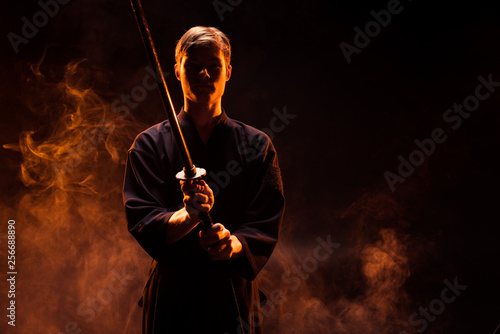 Young man in kimono holding kendo sword in smoke