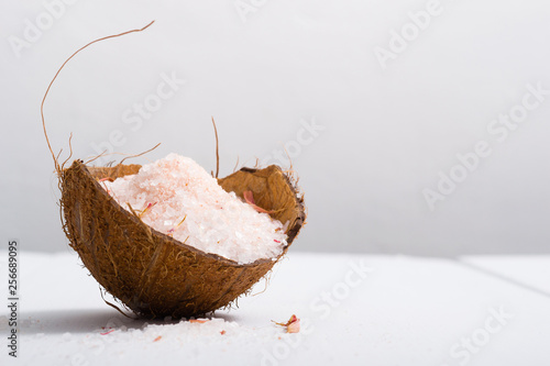 pile of pink bath salt at coconut shell bowl, white wood table
