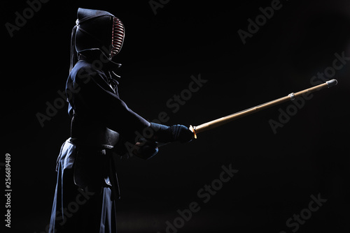 Fényképezés Kendo fighter in helmet holding bamboo sword on black