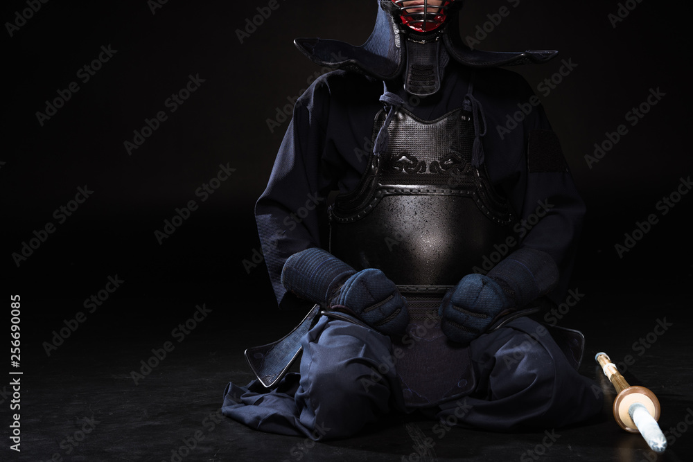 Partial view of kendo fighter in helmet with bamboo sword sitting on black Partial view of kendo fighter in helmet with bamboo sword sitting on black