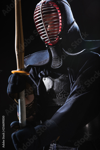 Kendo fighter in helmet holding bamboo sword isolated on black