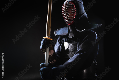 Kendo fighter in helmet holding bamboo sword on black