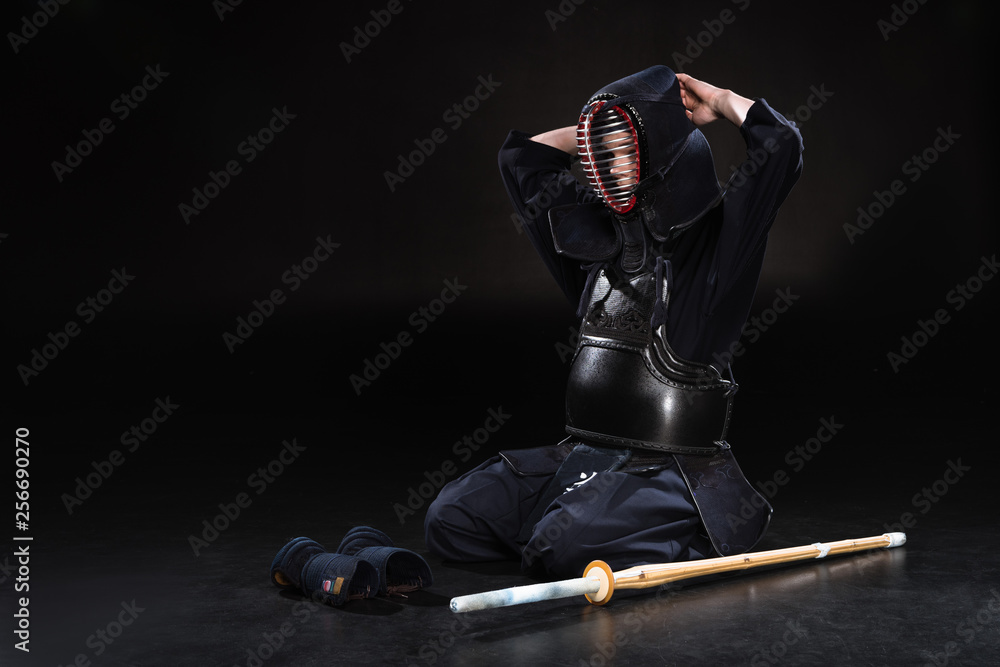 Fotografie Kendo fighter sitting on floor and taking off helmet on black