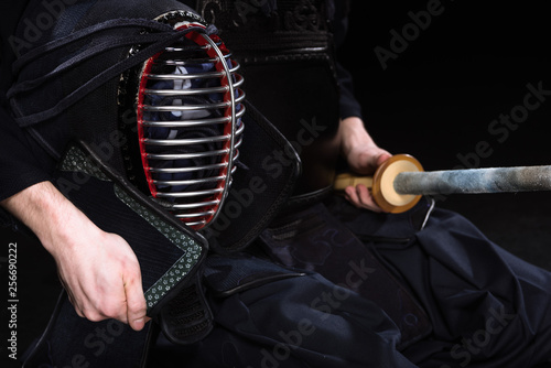 Bilde på lerret Cropped view of kendo fighter holding helmet and bamboo sword on black