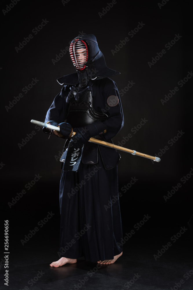 Naklejka premium Full length view of kendo fighter in helmet holding bamboo sword on black